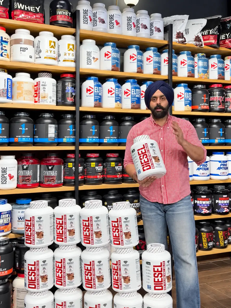 The owner of ARSH Supplements holding a tub of protein in front of the store's stocked shelves